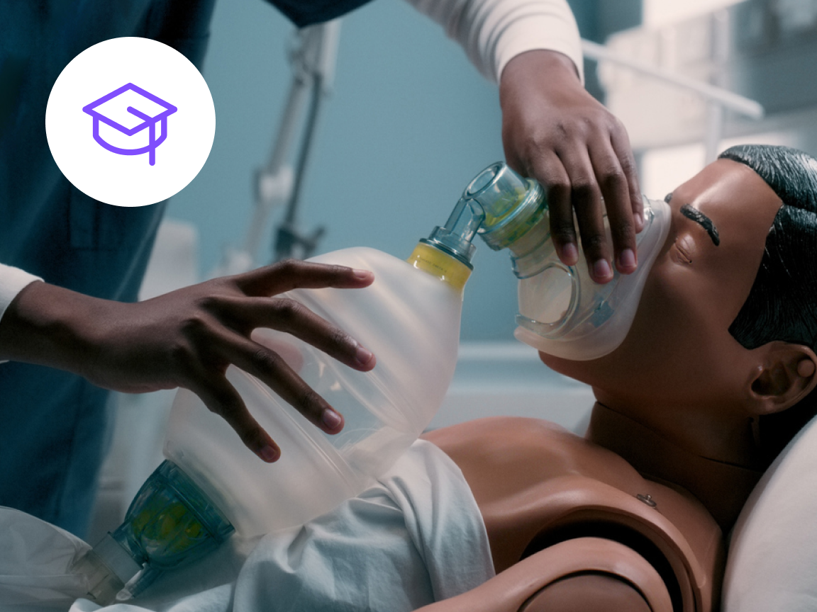 Healthcare professional applying a respirator to a patient mannequin during in-person clinical training in a hospital setting.